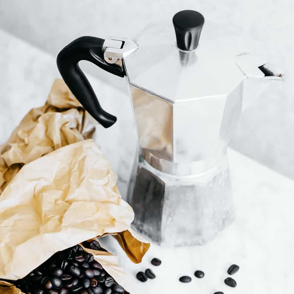 silver pot of coffee beside spilled coffee beans 