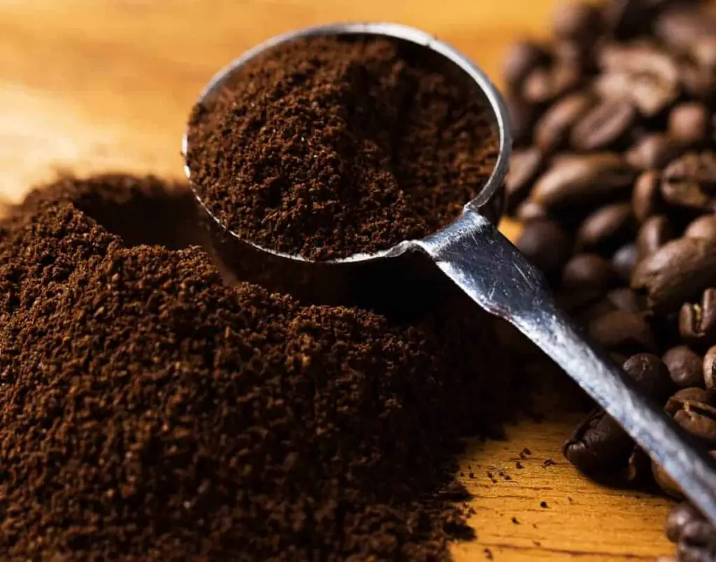 instant coffee in metal spoon with coffee beans on table in background