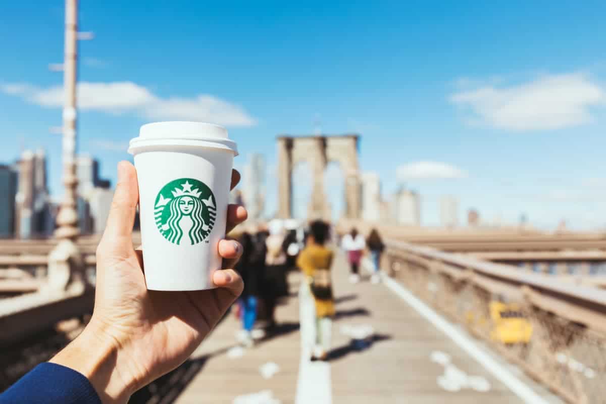 man holding Starbucks cup overlooking bridge