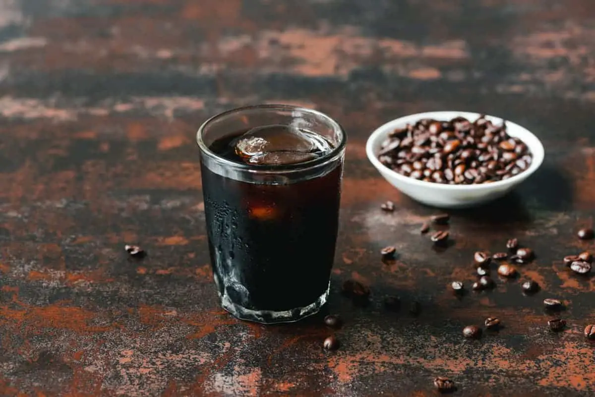 cold brew on ice in glass on rustic table near coffee beans.