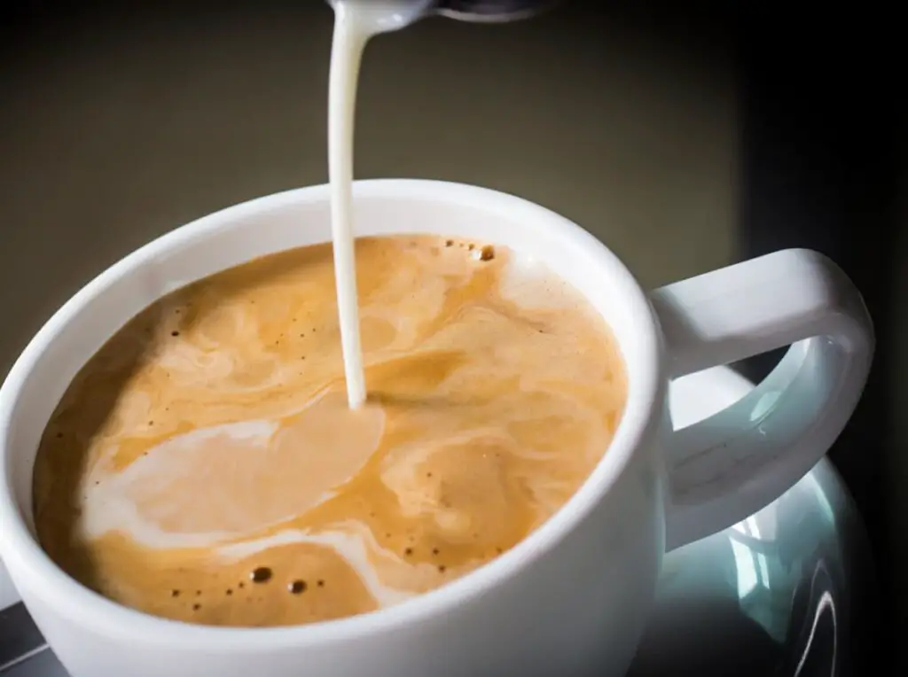 creamer pouring into coffee mug with dark background