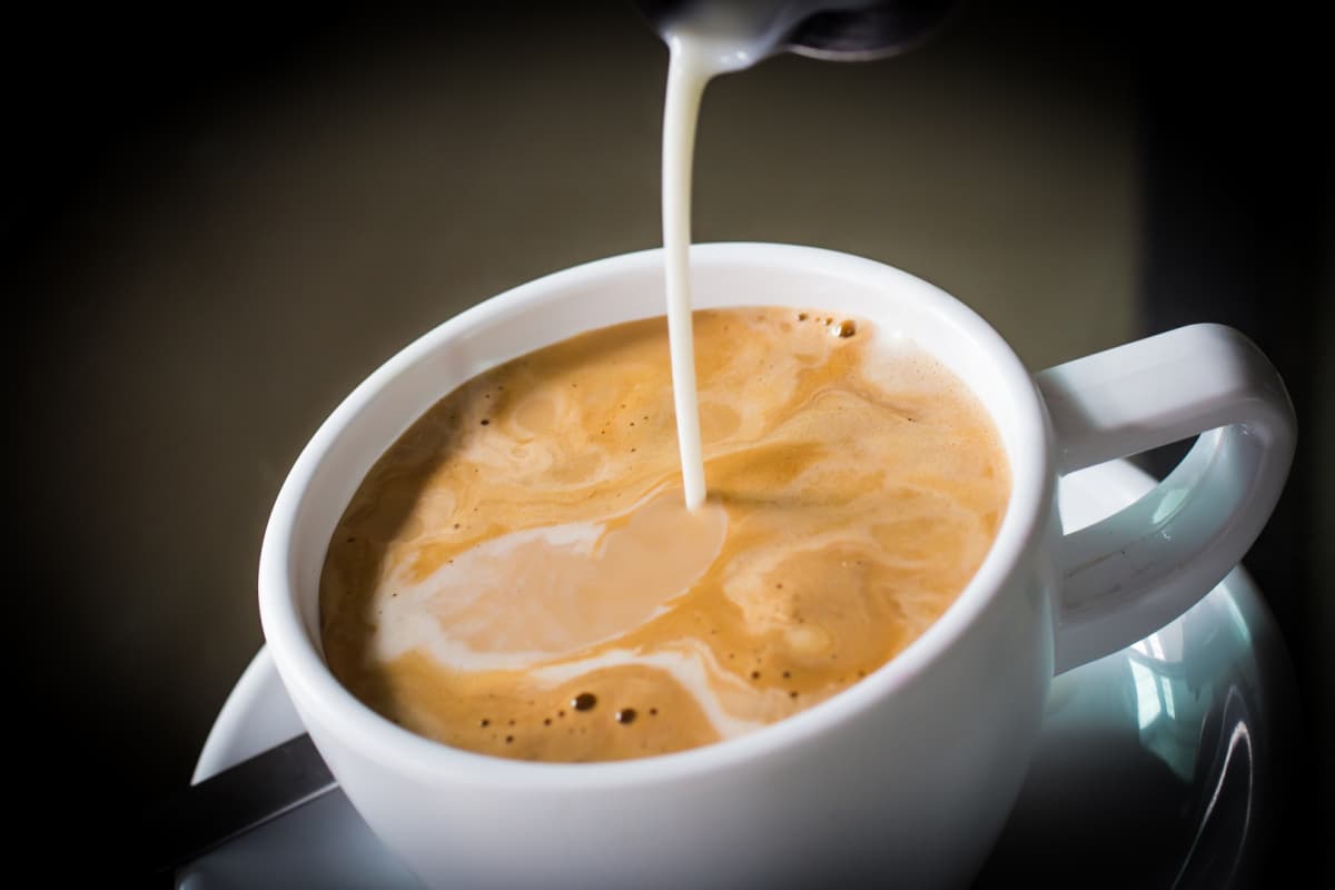 creamer pouring into white coffee mug with coffee; black background