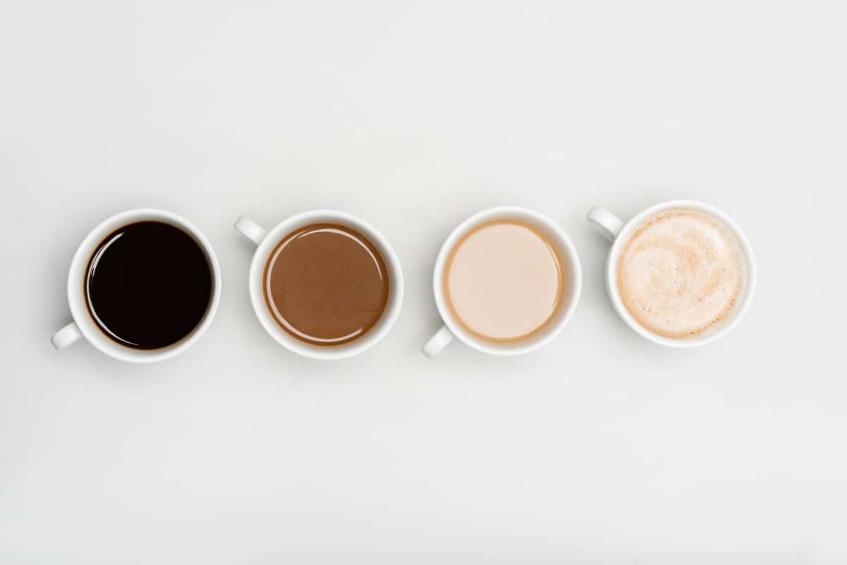 4 white coffee cups with different types of coffee with milk in some