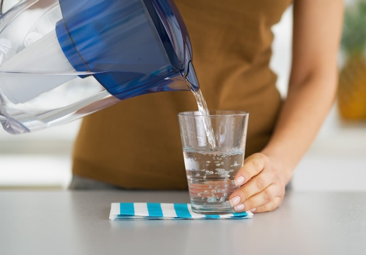 A woman pouring filtered water from a pitcher to a glass.