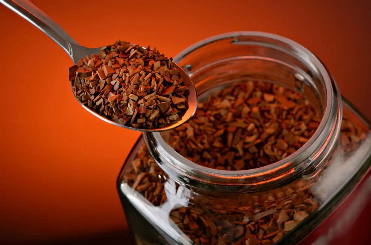 spoonful of instant coffee over jar with orange background