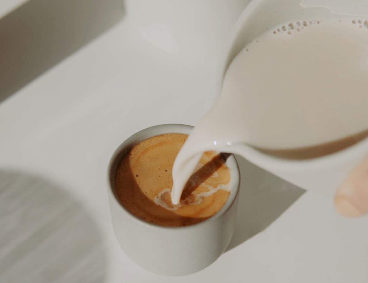 pouring milk in a cup of hot coffee