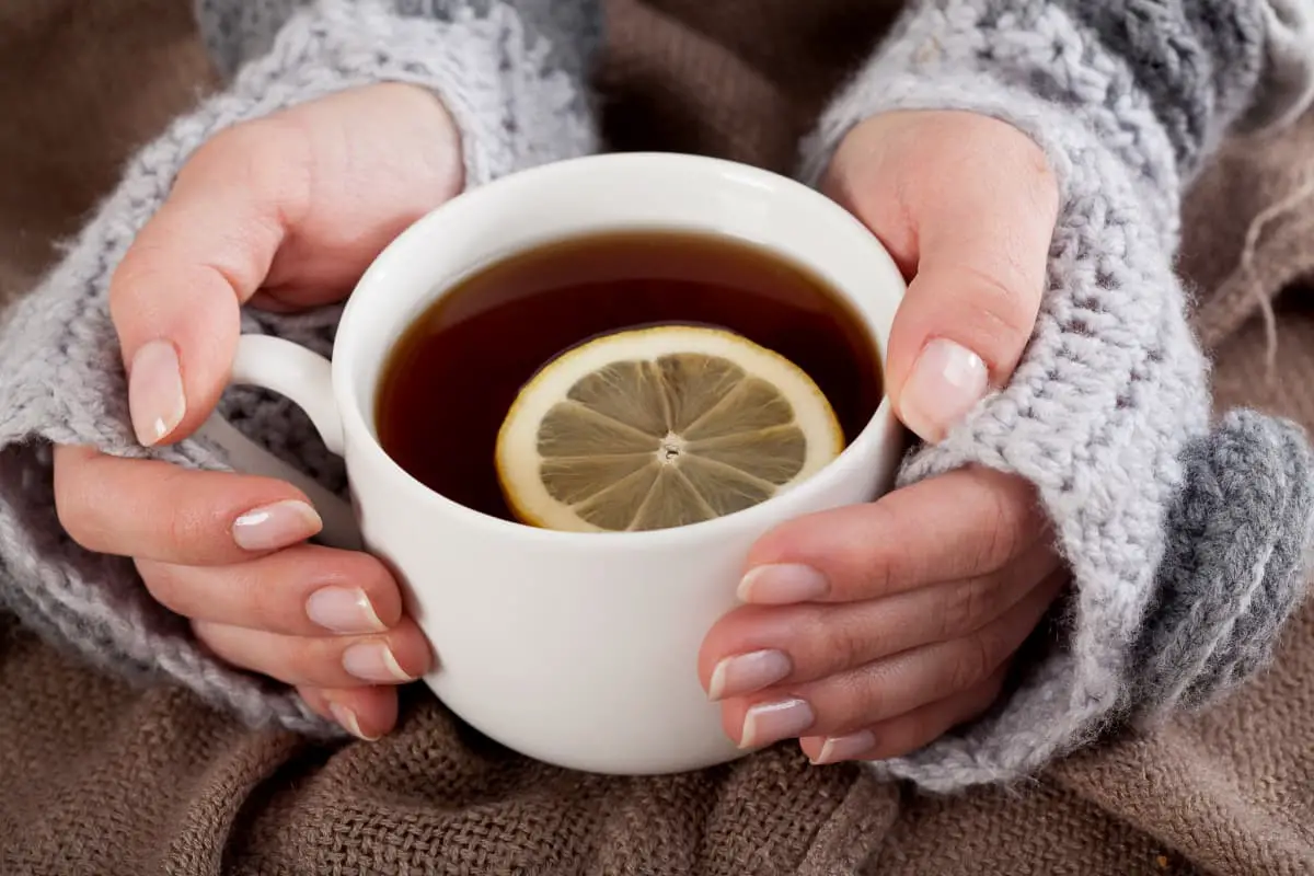 woman with chunky knit sweater holding cup of tea with slice of lemon inside mug