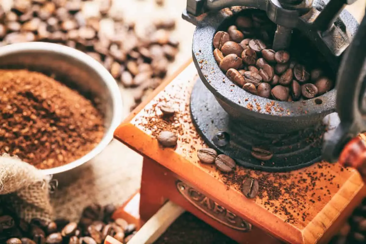 Whole coffee beans in manual coffee grinder with ground coffee to the side.