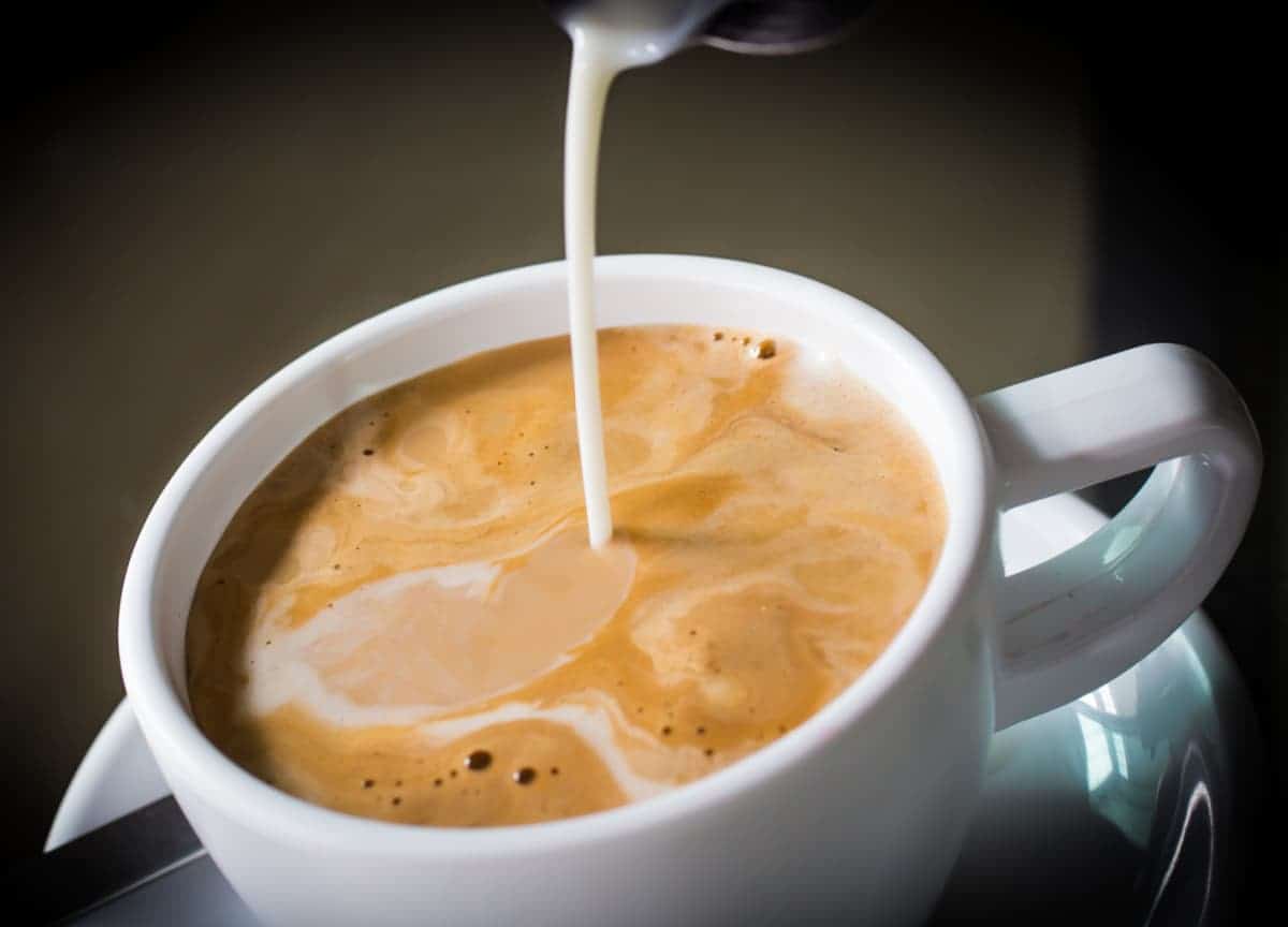 Coffee creamer pouring in white coffee mug.