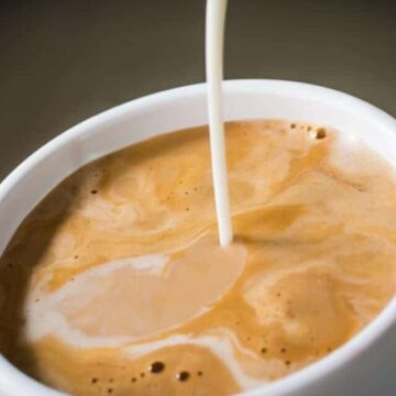Coffee creamer being poured into coffee in white mug.