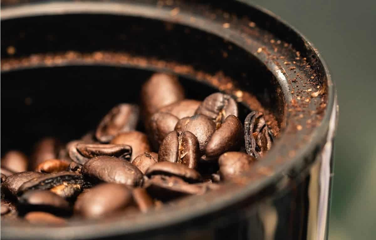Coffee beans in coffee grinder with ground coffee all over top.