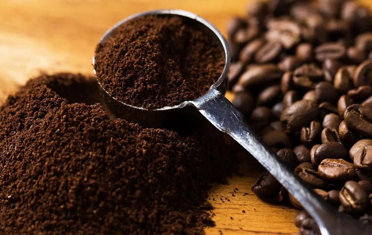 Instant coffee pile beside pile of whole coffee beans with scoop of coffee overflowing.