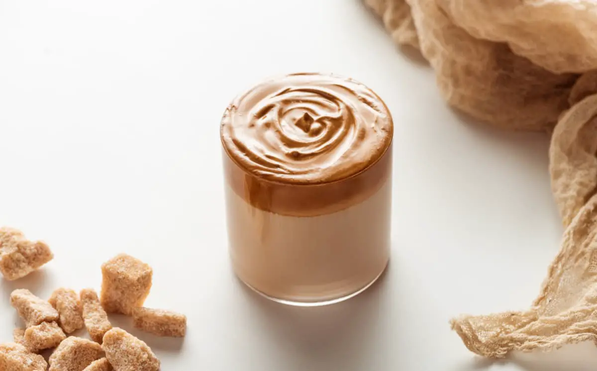 Whipped coffee beverage sitting on white background surrounded by other treats.