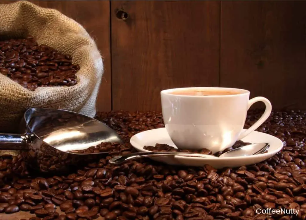 Coffee beans spilled out on table near bag, scoop and cup of coffee.