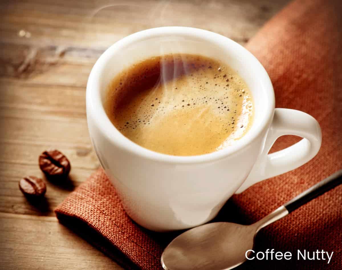 Espresso in white mug on napkin near spoon with coffee beans on wooden table.