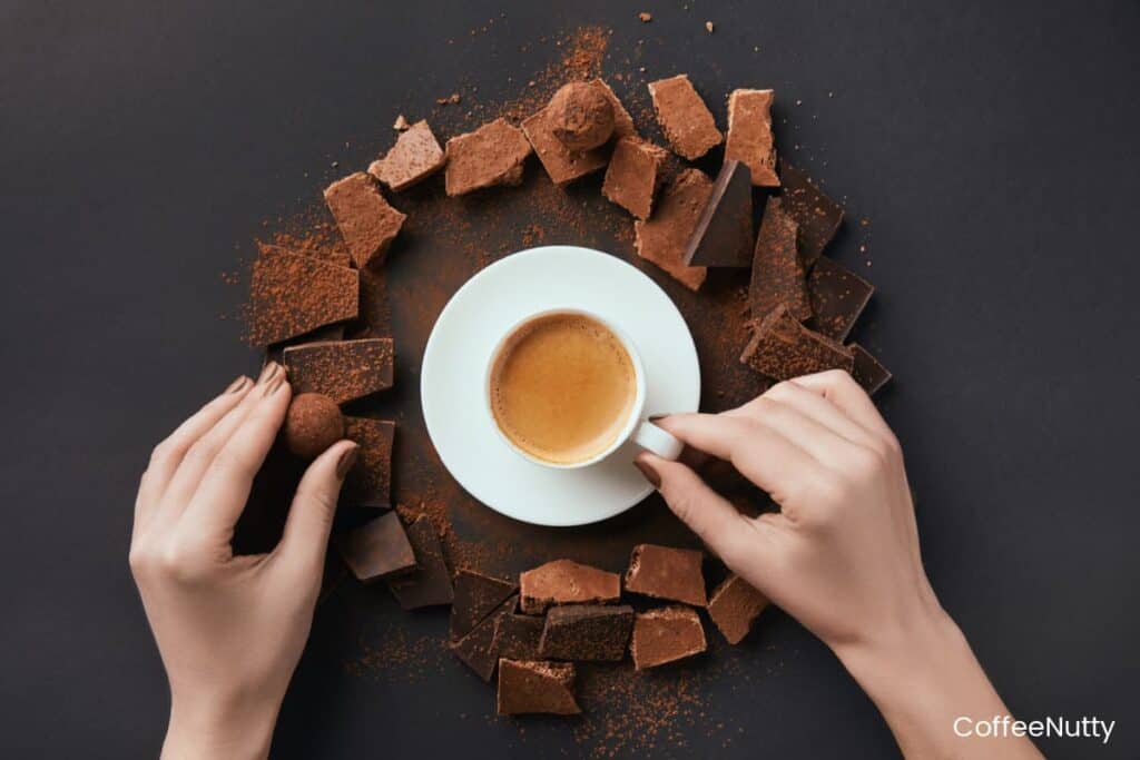 Pieces of chocolate surrounding white saucer with small cup of coffee.