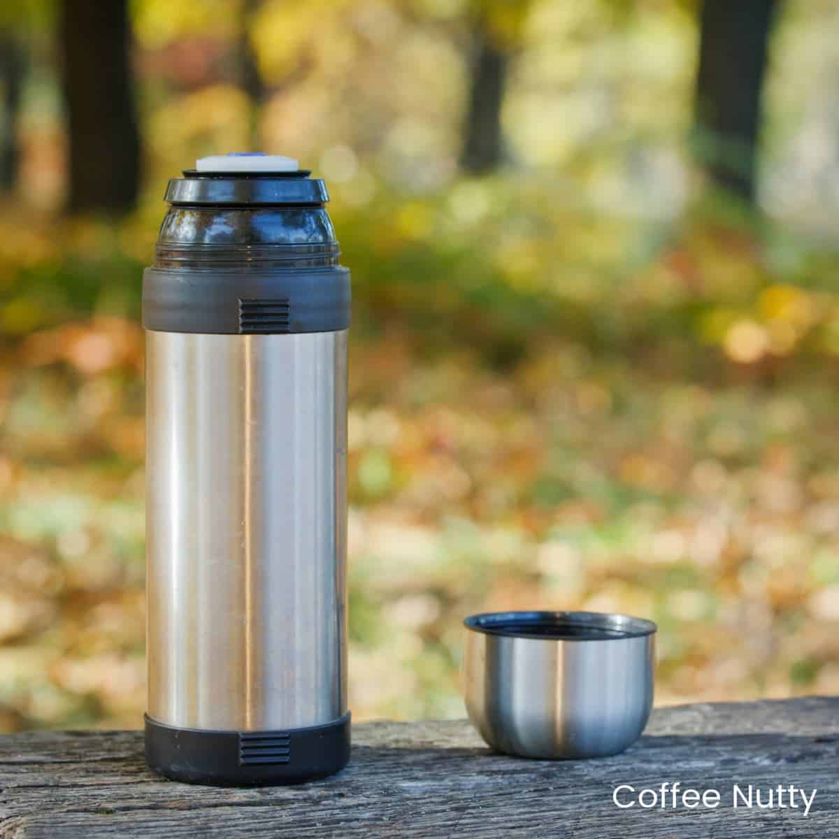 Coffee thermos and lid with blurred background of autumn leaves.