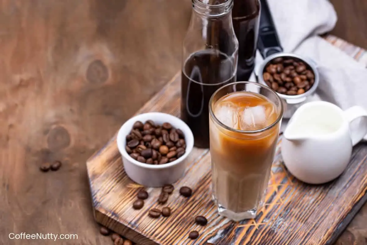 Glass of cold brew on table with coffee beans and milk.