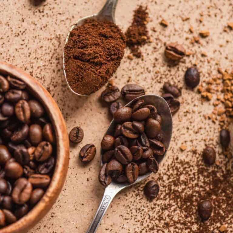 Two spoons on table with instant coffee in one and whole bean coffee in the other.