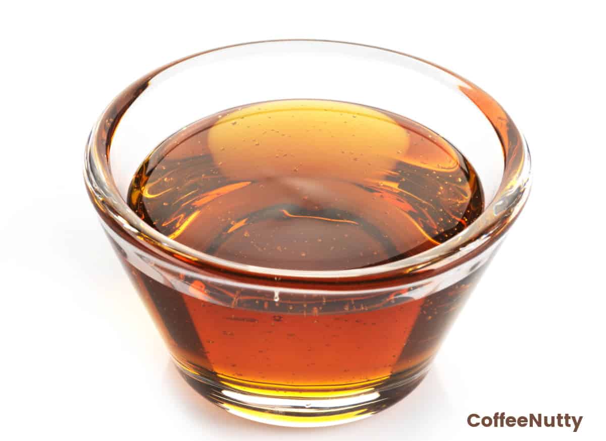 Amber colored syrup in small glass with white background.