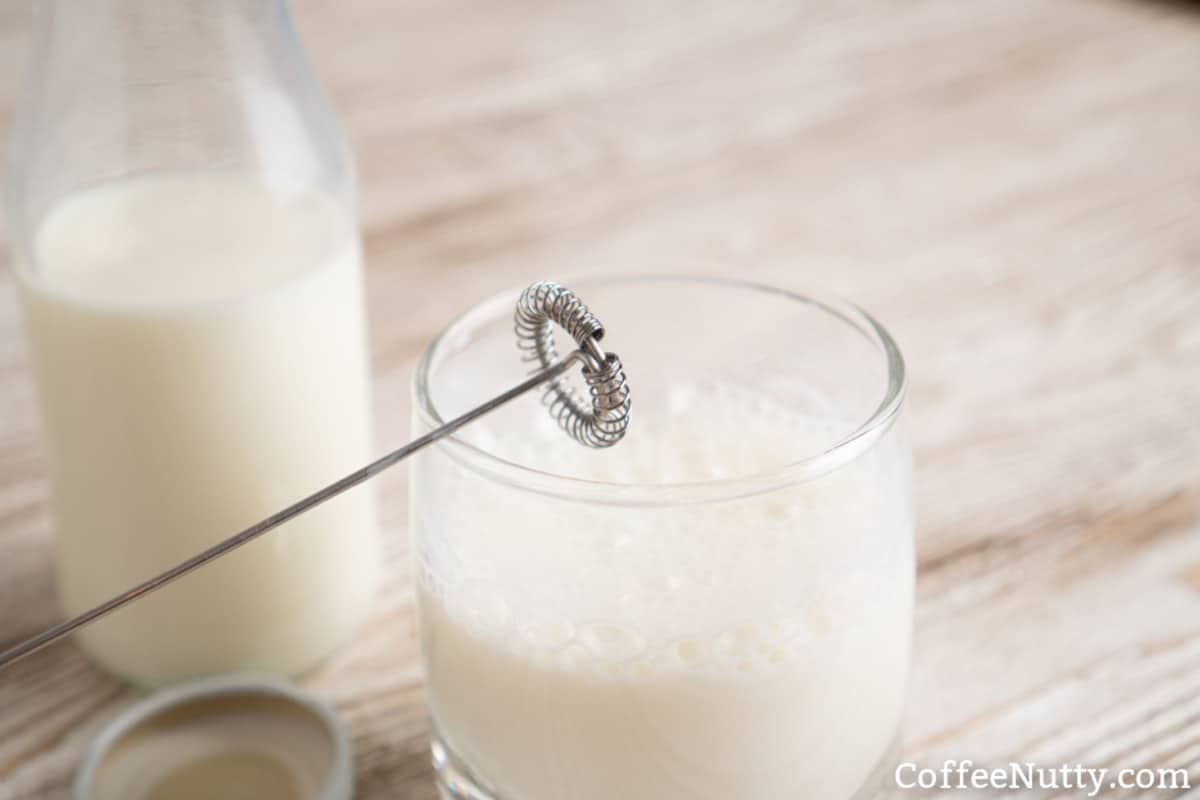 Milk sitting on wood table with frother in glass.