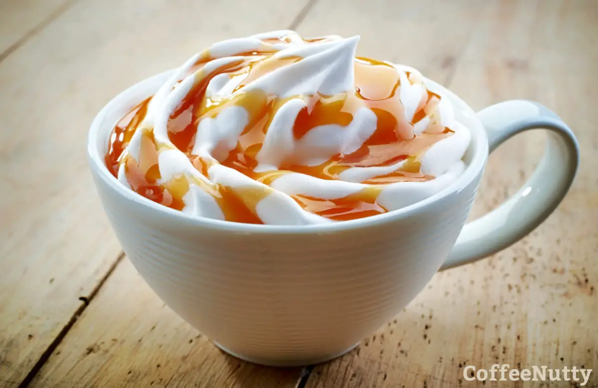 Caramel latte with whipped cream in white mug.