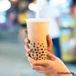 Coffee milk tea with tapioca pearls in cup held by woman.