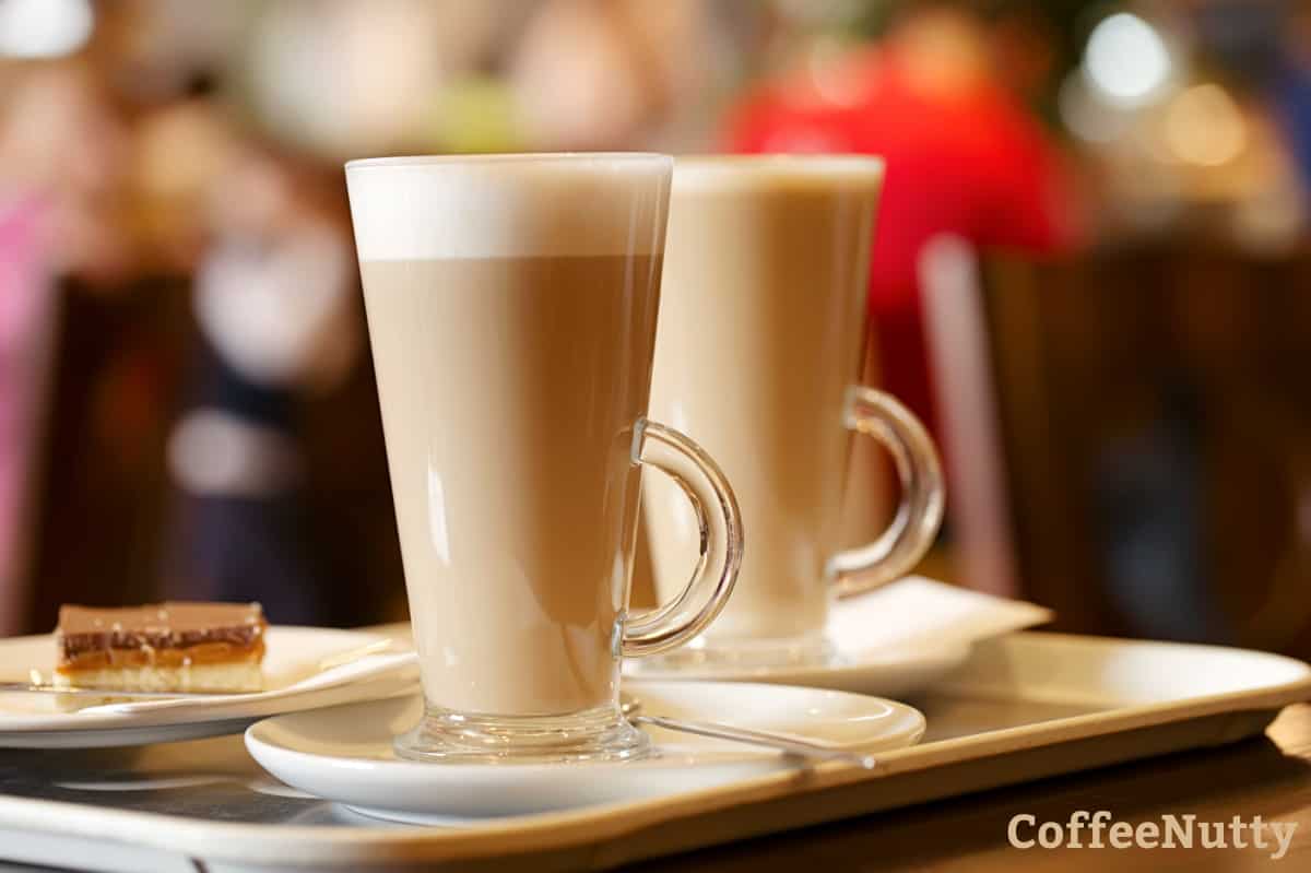 Two glasses of lattes sitting on table near dessert.