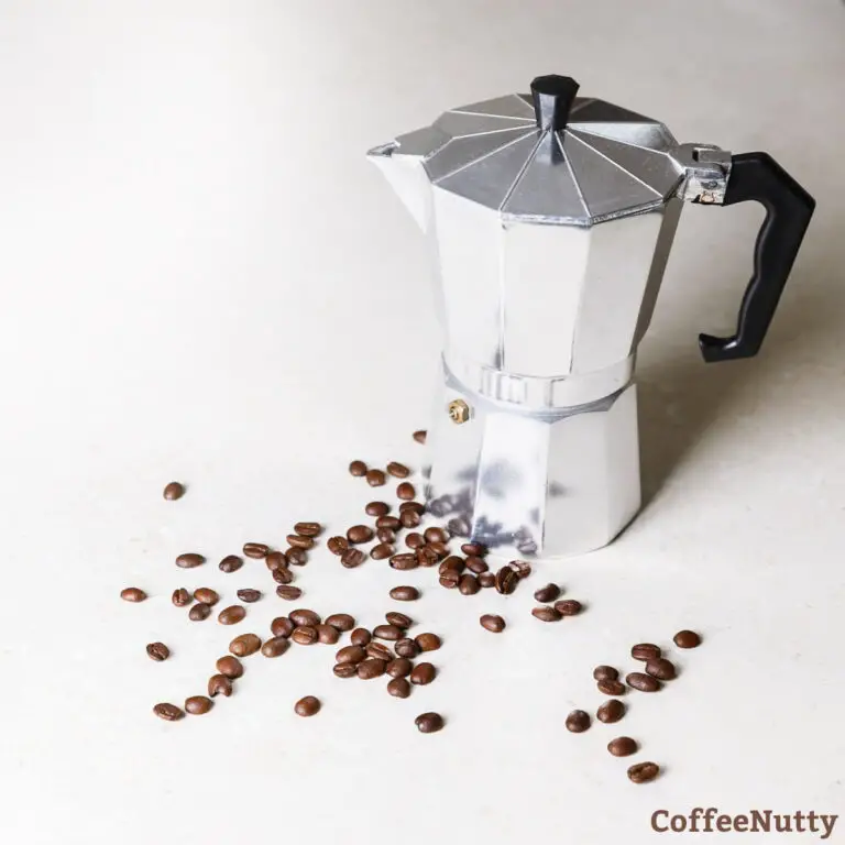 Stainless steel moka pot on table with coffee beans.