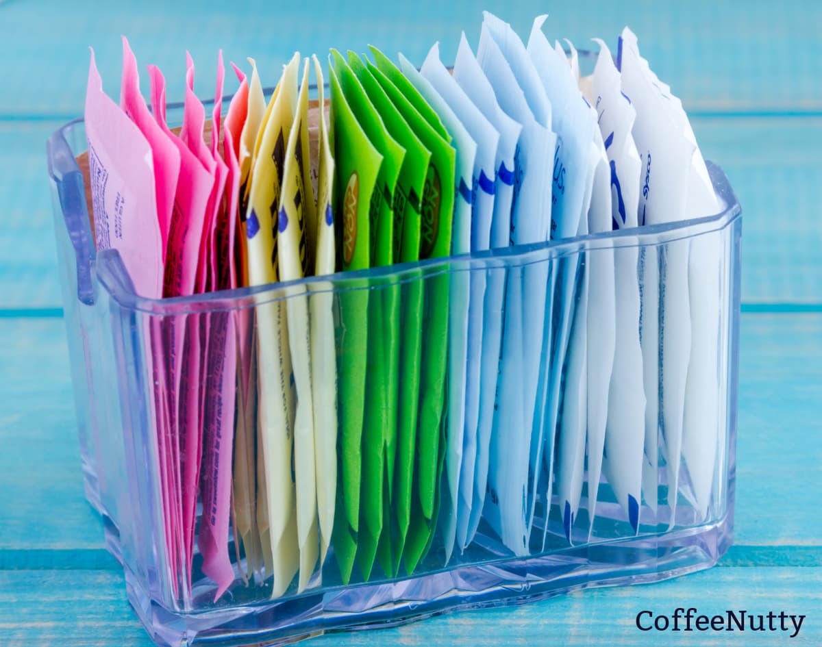 Variety of artificial sweeteners in clear container on table.