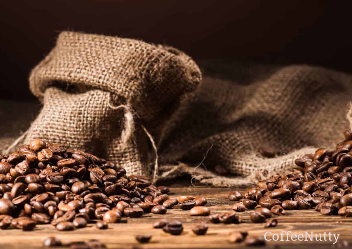 Coffee beans in burlap sacks, spilled along wooden table.