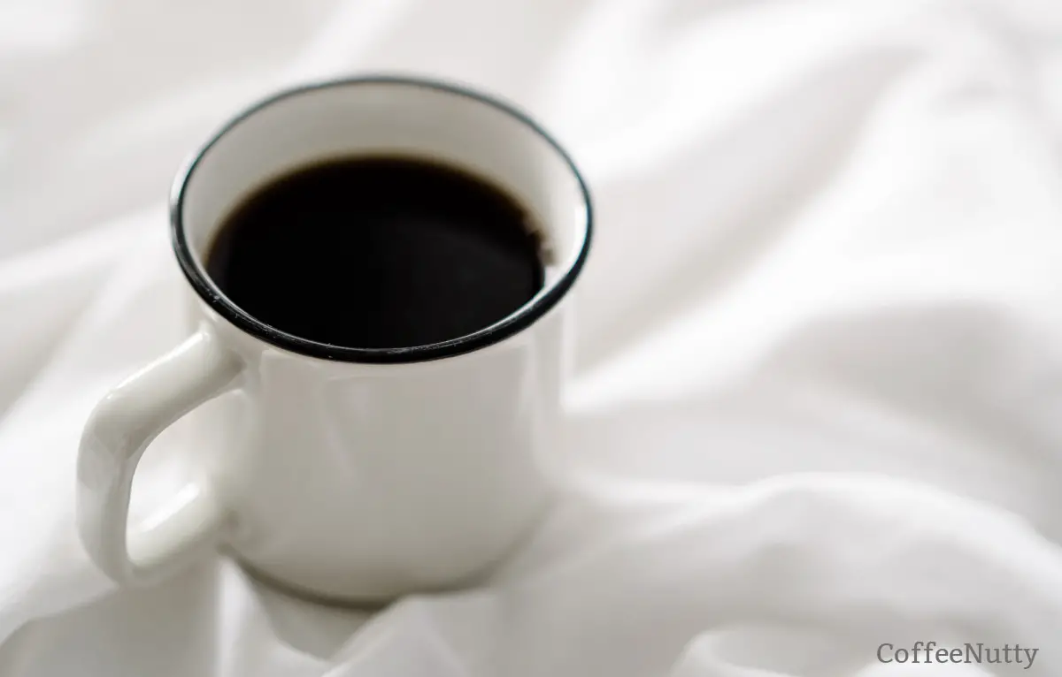 Cup of coffee in white mug on white fabric background.