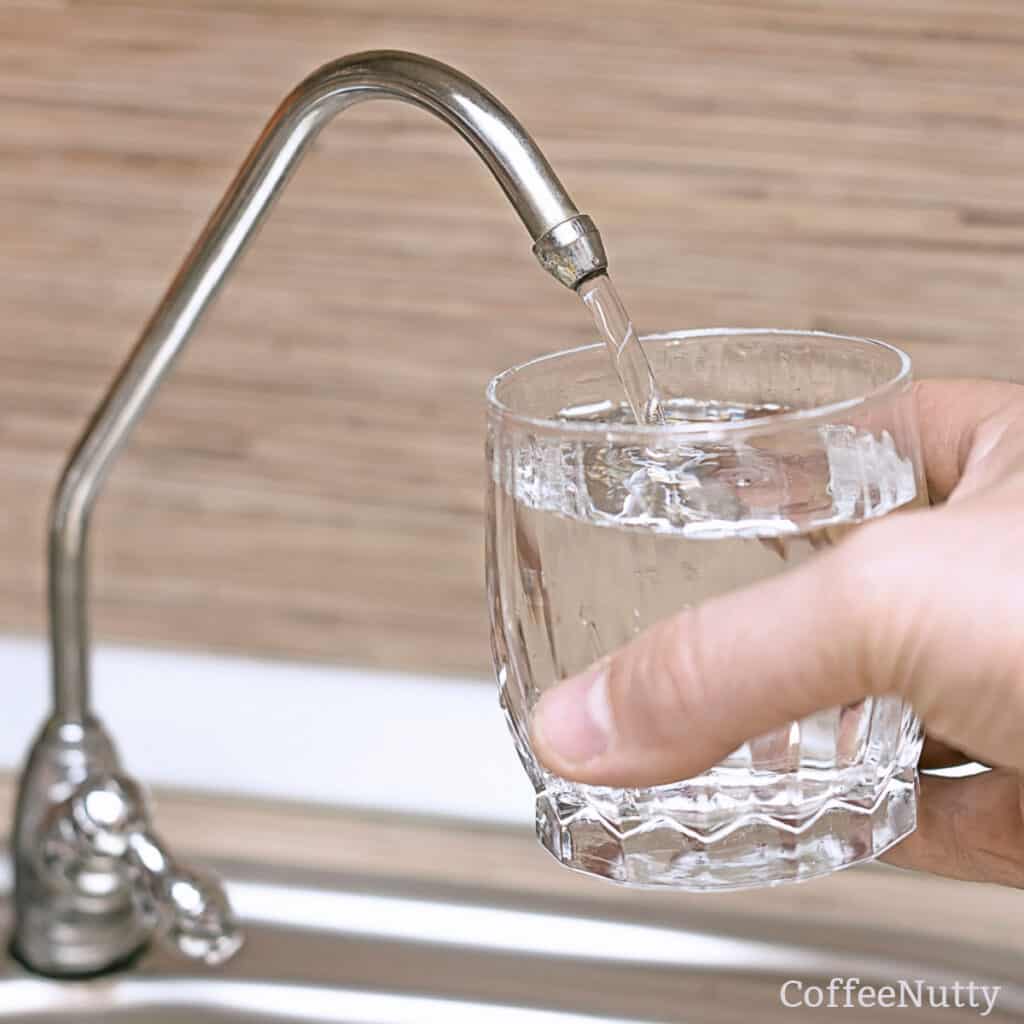 Man holding glass under water filter system and filling glass to top.