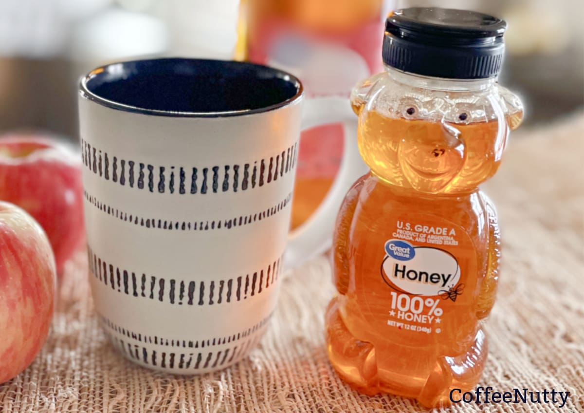 Bottle of honey beside cup of coffee.