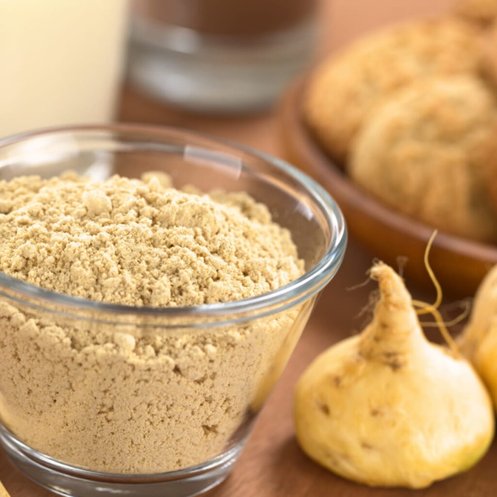 Maca powder in glass jar beside maca root on wood table.