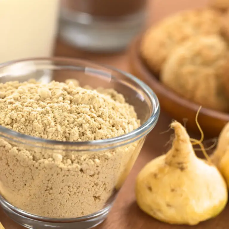 Maca powder in glass jar beside maca root on wood table.