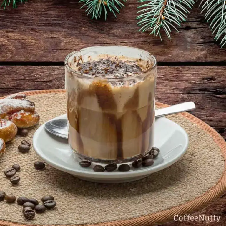 Mocha in clear glass sitting on white saucer beside spoon.