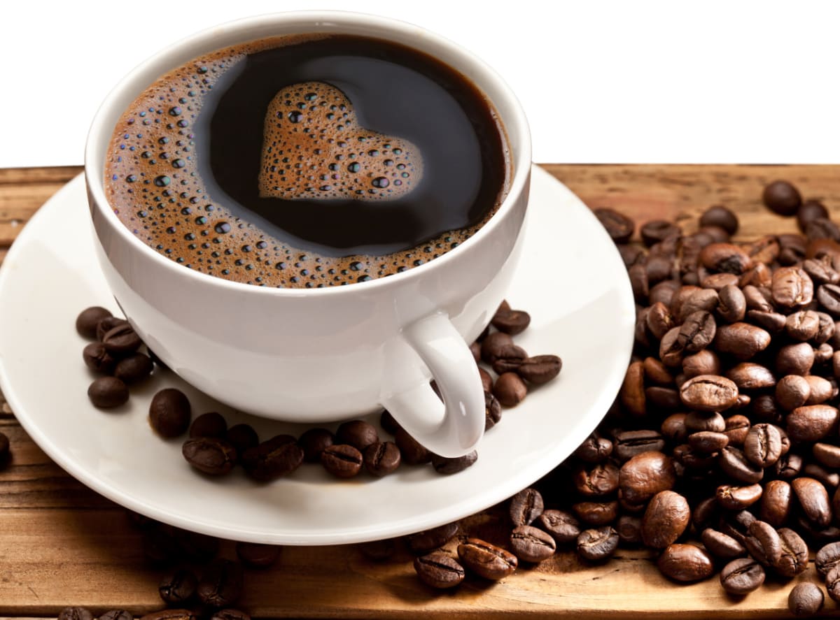 Coffee in white mug beside coffee beans on wood table.