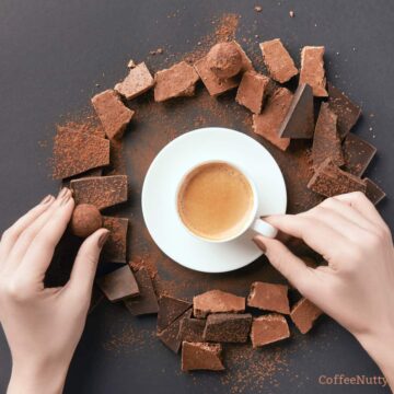 Cacao and coffee on table with woman's hand holding white mug.
