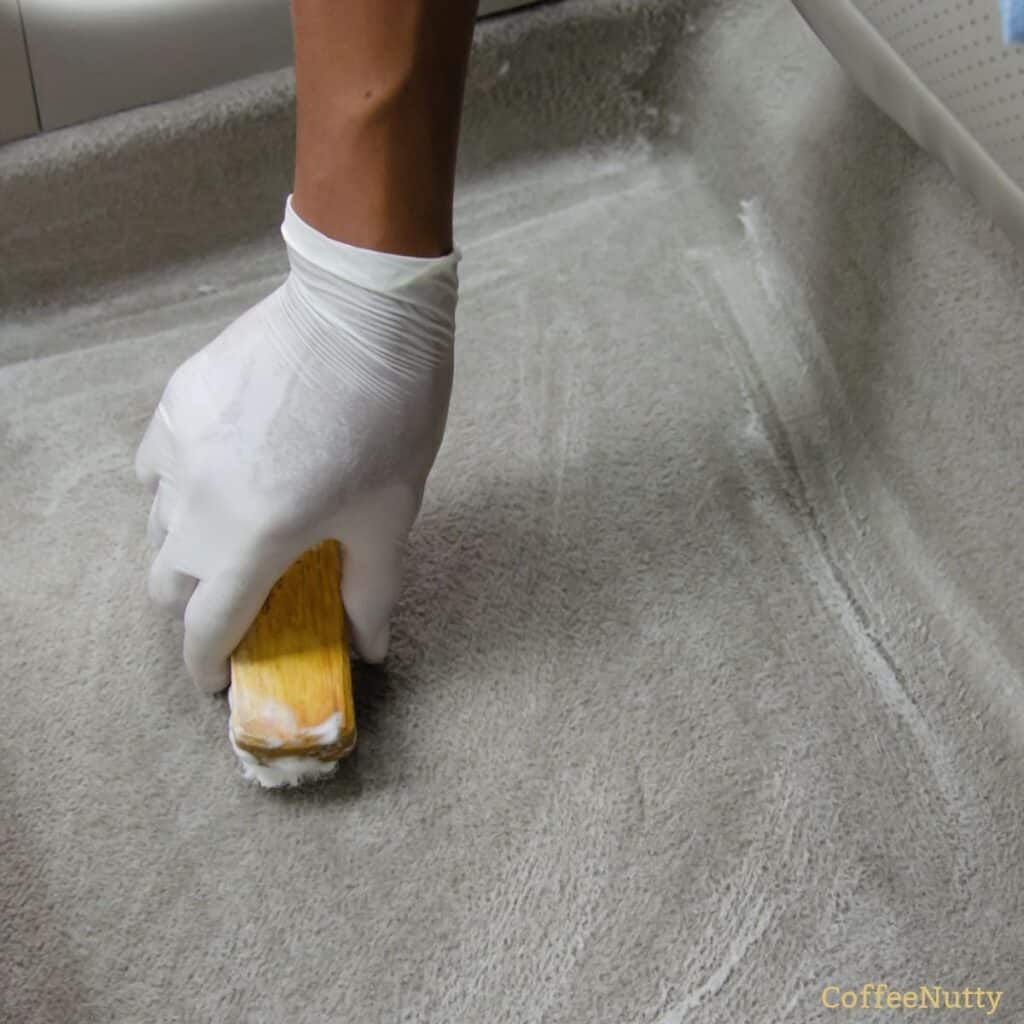 Scrubbing stains from car carpet with carpet cleaner and scrub brush.