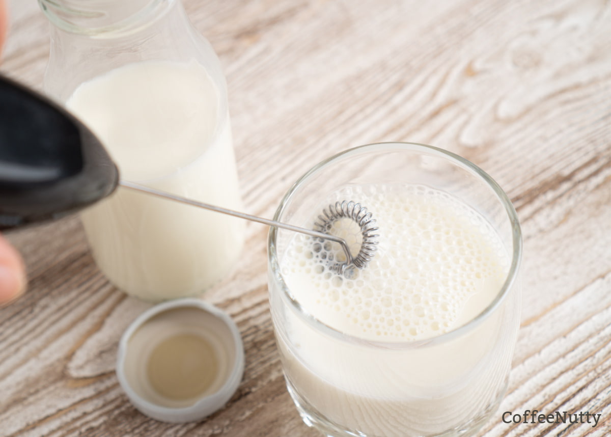 Handheld milk frother in a cup of milk in clear glass.