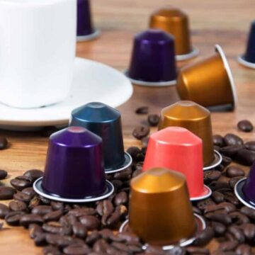 Nespresso capsules beside coffee mug and coffee beans.