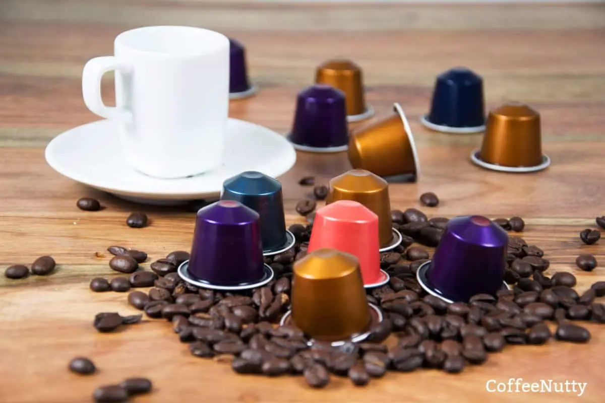 Nespresso Vertuo coffee capsules beside white coffee mug and coffee beans on table.